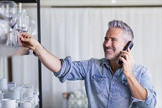 Caucasian man reaching for glassware talking on telephone