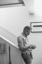Caucasian man leaning on staircase bannister texting on cell phone