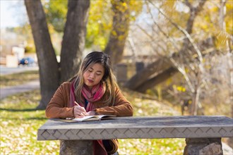 Asian woman writing in journal on table in autumn