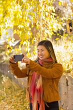 Asian woman posing for cell phone selfie in autumn