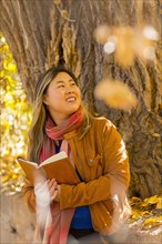 Smiling Asian woman reading book in autumn