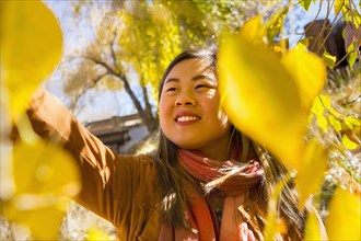 Smiling Asian woman reaching for leaf in autumn