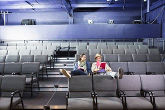 Caucasian actors sitting in audience with scripts in theater