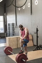 Mixed Race man resting on barbell in gymnasium
