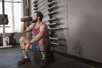 Mixed Race man drinking from bottle in gymnasium