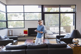 Caucasian man standing in livingroom using digital tablet