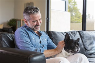 Caucasian man sitting on sofa petting dog