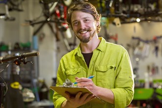 Smiling Caucasian worker writing on clipboard in bicycle shop