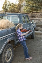 Caucasian girl leaning on truck playing violin