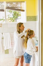 Caucasian mother brushing hair of daughter in bathroom