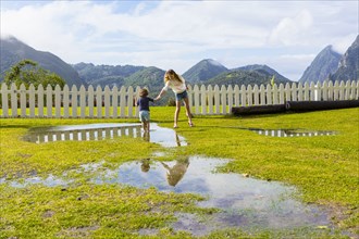 Caucasian girl helping brother standing in puddle