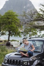 Caucasian girl sitting on hood of car reading map