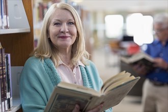 Smiling Caucasian woman holding book in library