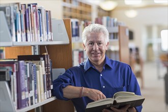 Smiling Hispanic man holding book in library