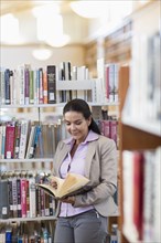Smiling Hispanic woman reading book in library