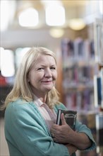 Smiling Caucasian woman holding book in library