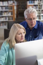 Older man helping woman with computer in library