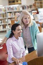 Older woman helping woman using computer in library