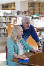 Older man helping woman using computer in library