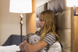 Frustrated Caucasian girl holding stuffed animals on hotel bed
