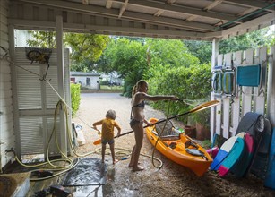 Caucasian brother and sister rinsing kayak with hose