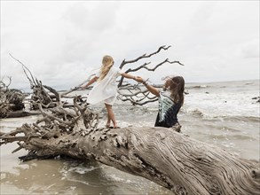 Caucasian mother and daughter walking on driftwood on beach