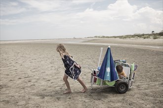 Girl pulling brother in cart on beach