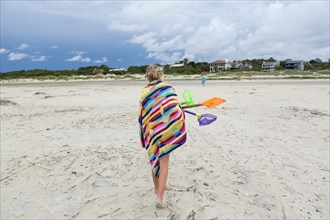 Caucasian girl walking on beach carrying net and shovels