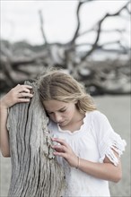 Caucasian girl examining driftwood on beach