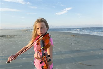 Caucasian girl playing violin on windy beach
