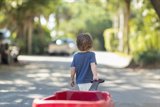 Caucasian boy pulling red wagon in street