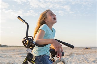 Laughing Caucasian girl leaning on bicycle at beach