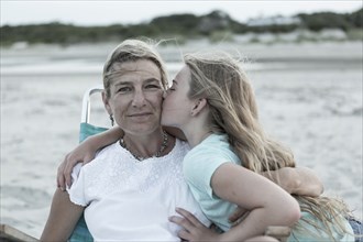 Caucasian girl kissing mother on cheek at windy beach