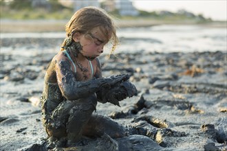 Caucasian girl covered in mud playing on beach