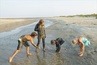 Caucasian brother and sisters covered in mud playing on beach
