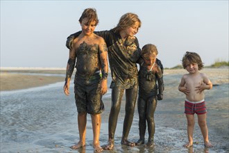 Caucasian brothers and sisters covered in mud standing on beach