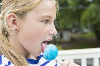 Tongue of Caucasian girl licking blue lollipop