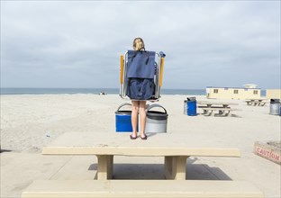 Caucasian girl carrying folding chair on picnic table at beach