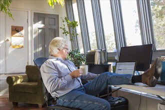 Caucasian man drinking coffee and using laptop with feet up on desk