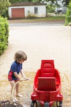 Caucasian boy washing red wagon with hose