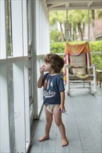 Curious Caucasian boy wearing diaper near screen door