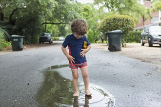 Caucasian boy standing in puddle on street