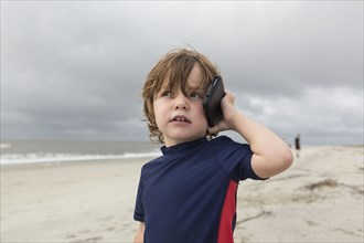 Caucasian boy talking on cell phone on beach