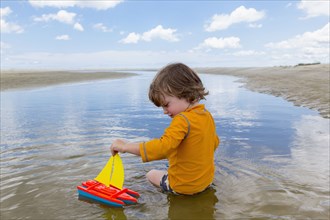 Caucasian boy sitting in water playing with toy sailboat