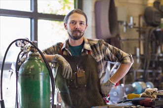 Confident Caucasian man leaning on gas tank in workshop