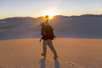 Caucasian man carrying camera and tripod in desert