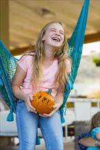 Laughing Caucasian girl in hammock holding pumpkin