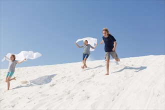 Caucasian boy and girls running on sand dune