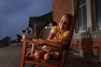 Family sitting in wooden rocking chairs at dusk