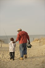 African father and son walking on beach with fishing gear
